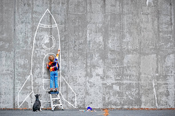 Een jongetje dat een raket tekent met krijt op een muur.